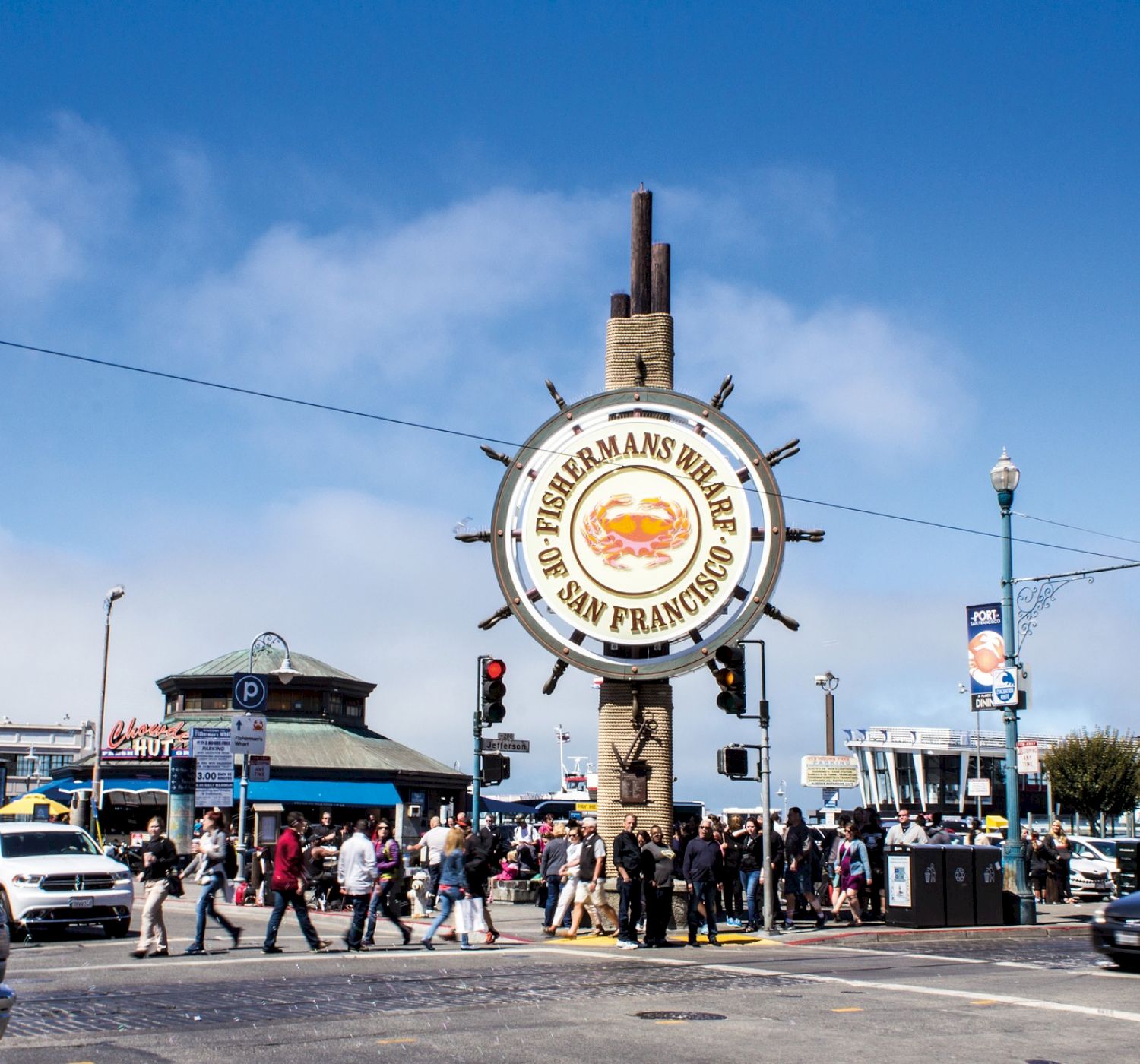 A bustling street scene in Fisherman's Wharf, San Francisco with people and cars passing by, featuring the iconic Fisherman's Wharf sign.